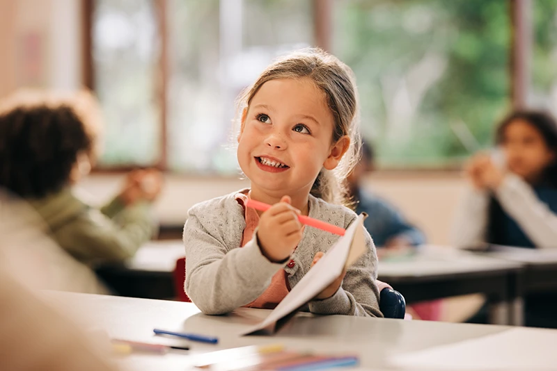 a little girl smiling at school and drawing