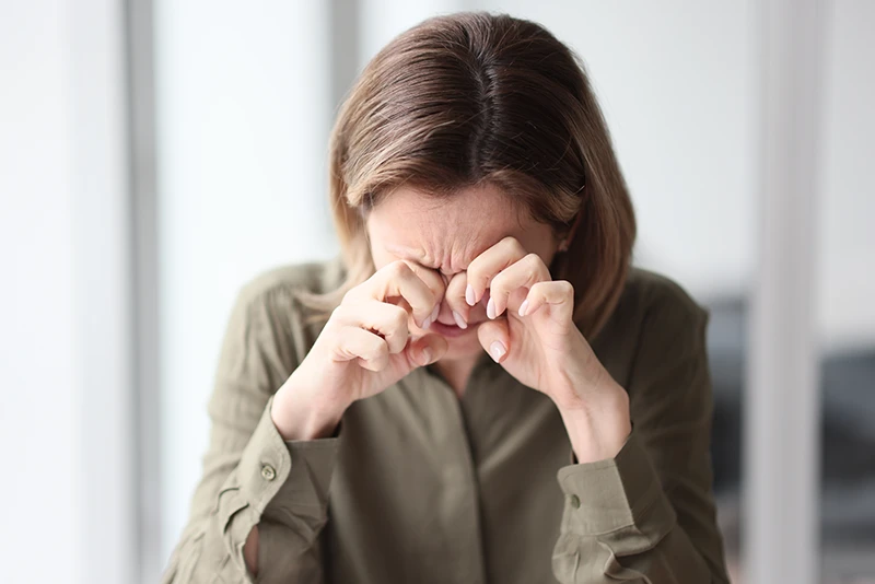 vision-therapy-for-adults a woman sitting down and holding her hands to her face in pain